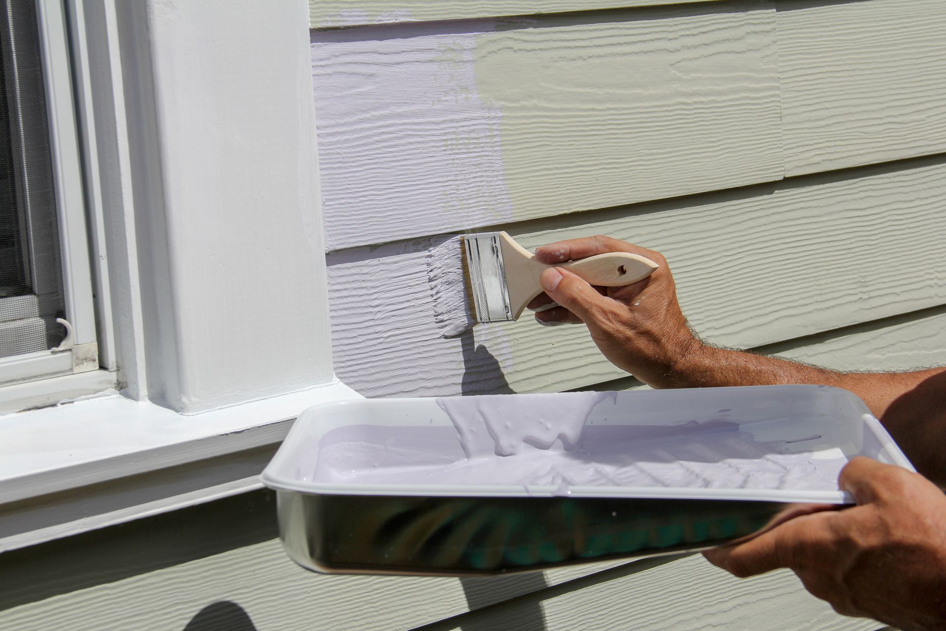 A person is painting a house with a brush and a tray of paint.