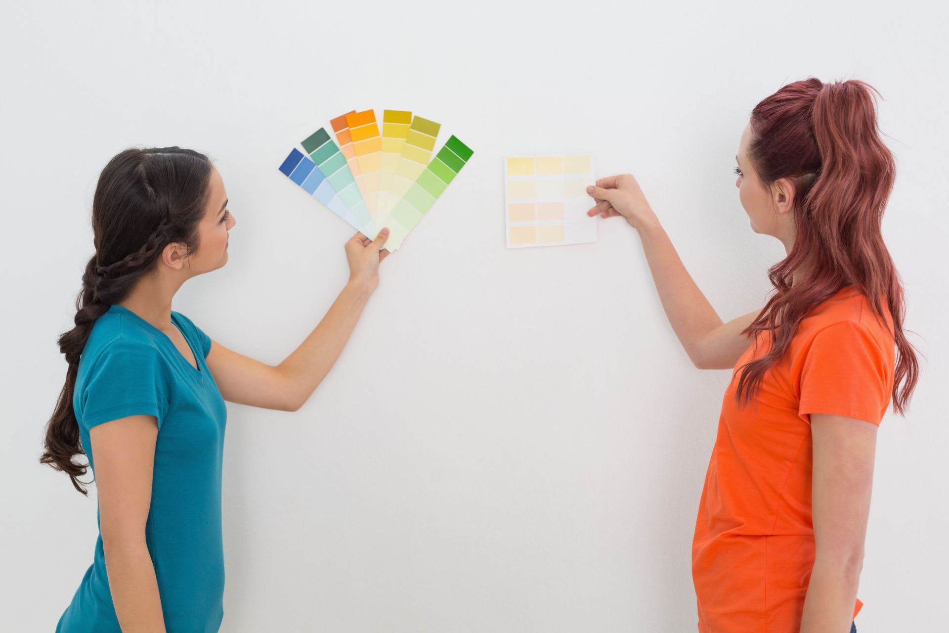 Two women are looking at paint samples on a wall.