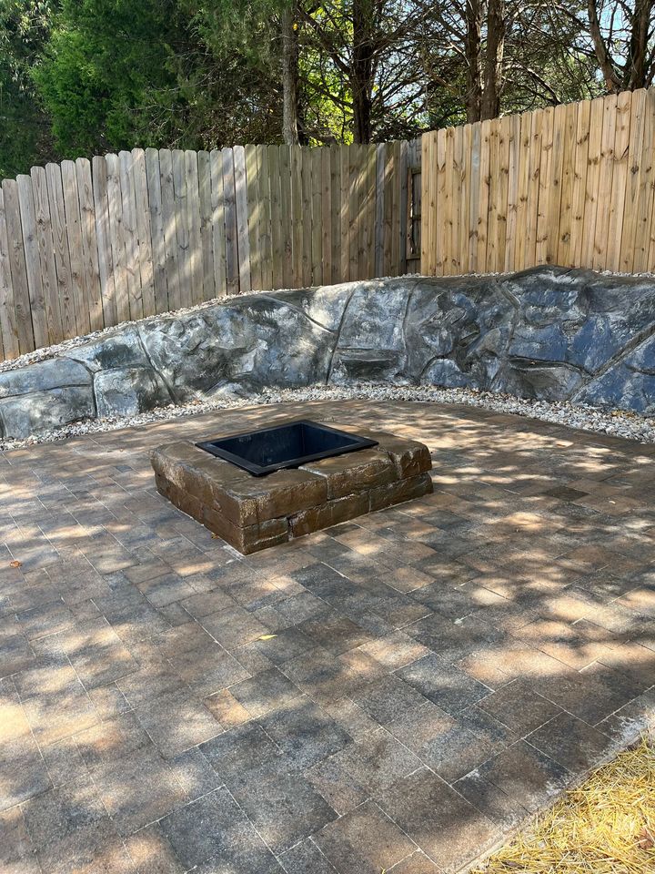 Backyard fire pit with stone seating area and wooden fence in dappled sunlight
