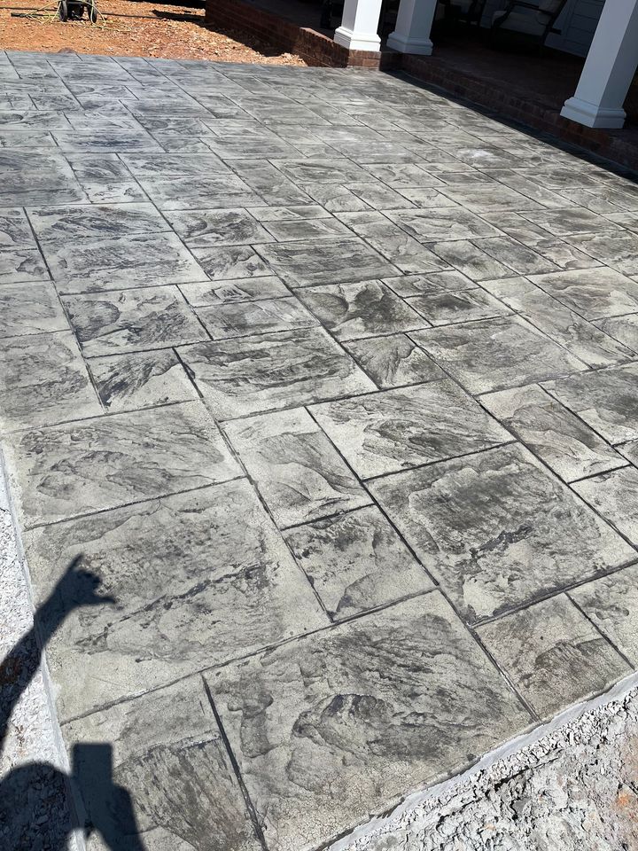 Stamped concrete patio with a light gray stone pattern and a person’s shadow in the lower left.