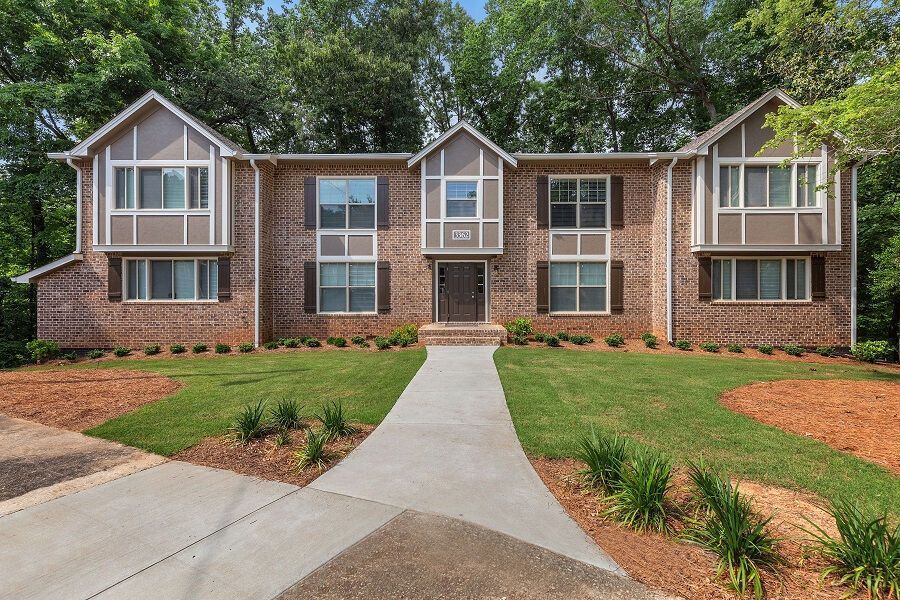 Brick apartment building with white-trimmed windows, central walkway, and landscaped lawn