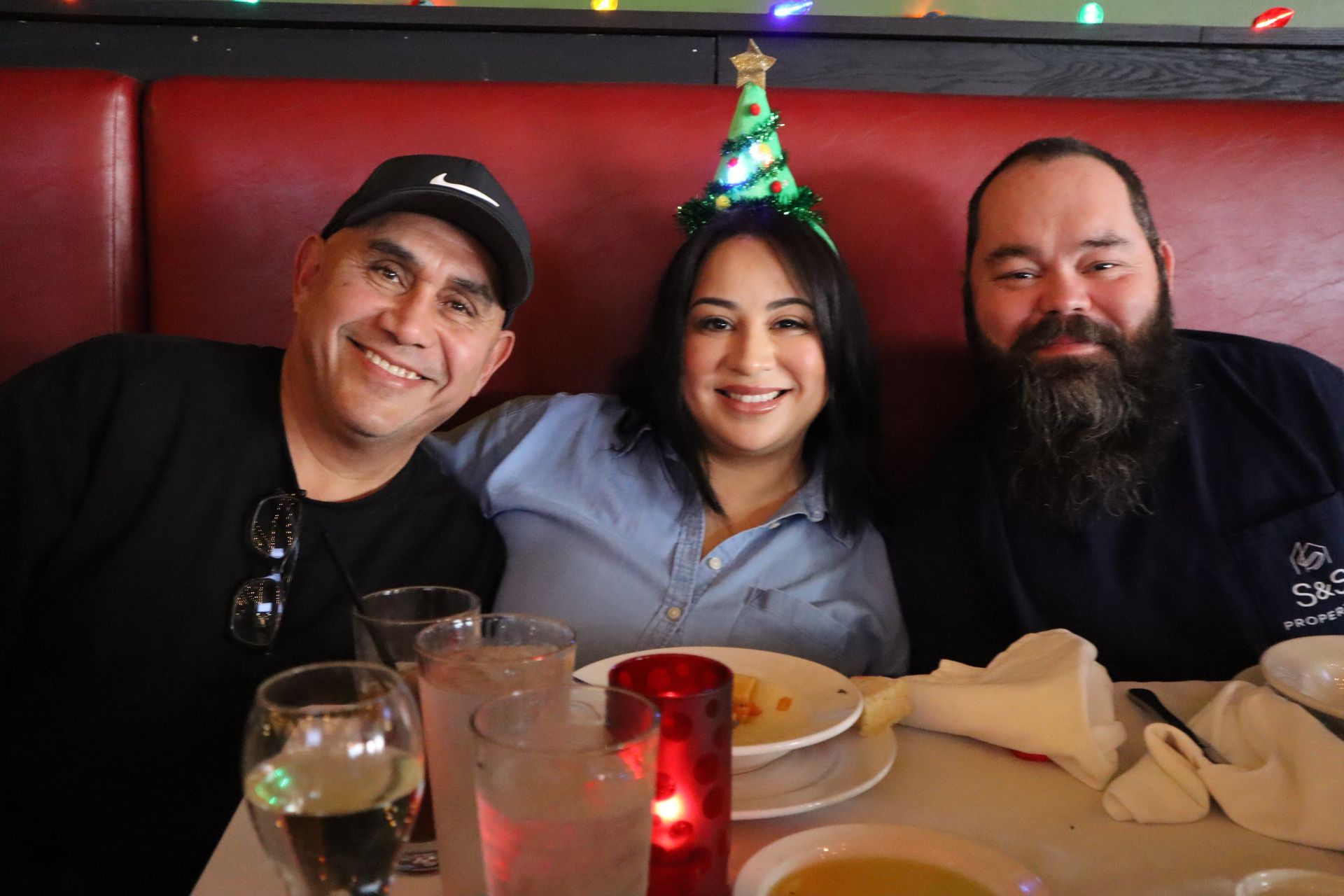 Three people smiling at a restaurant table, with a party hat and drinks in front of them.