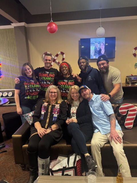 Group of people posing together in a festive room with holiday decorations and a TV in the background
