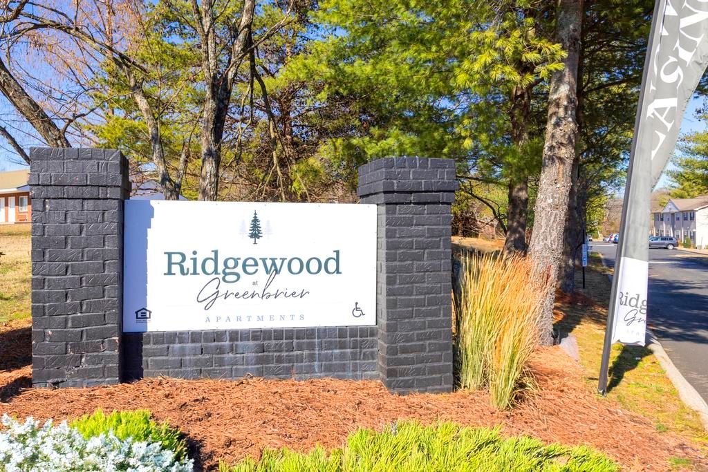 Ridgewood Apartments entrance sign beside trees, brick pillars, and landscaped mulch beds