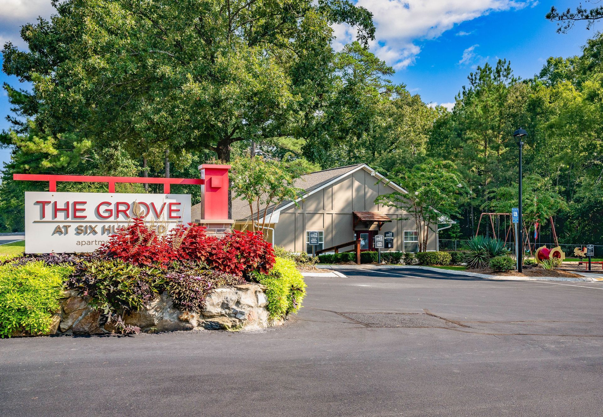 Entrance sign for The Grove apartment community beside landscaped flowers and trees under a blue sky