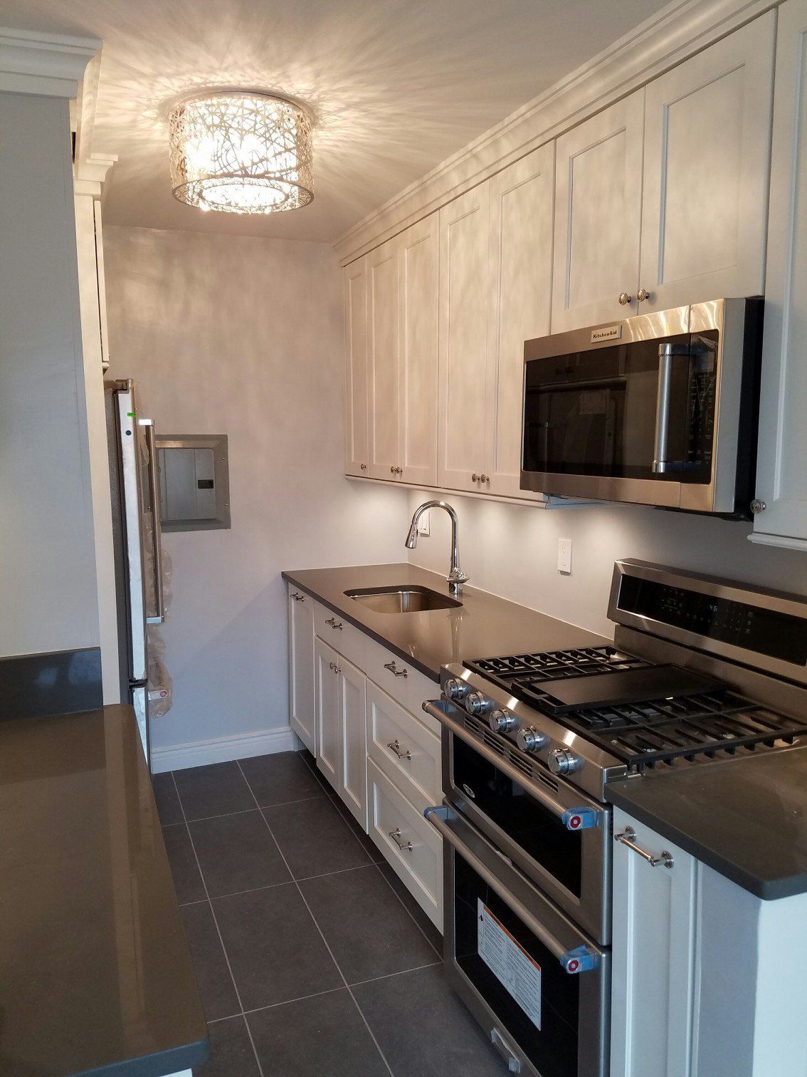 Kitchen remodel with dark gray tile floors, dark gray countertops, white cabinets and new appliances