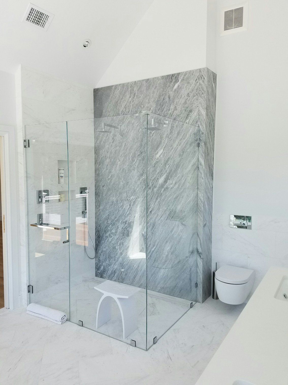 Bathroom remodel with all glass shower complete with white shower bench and gray stone wall