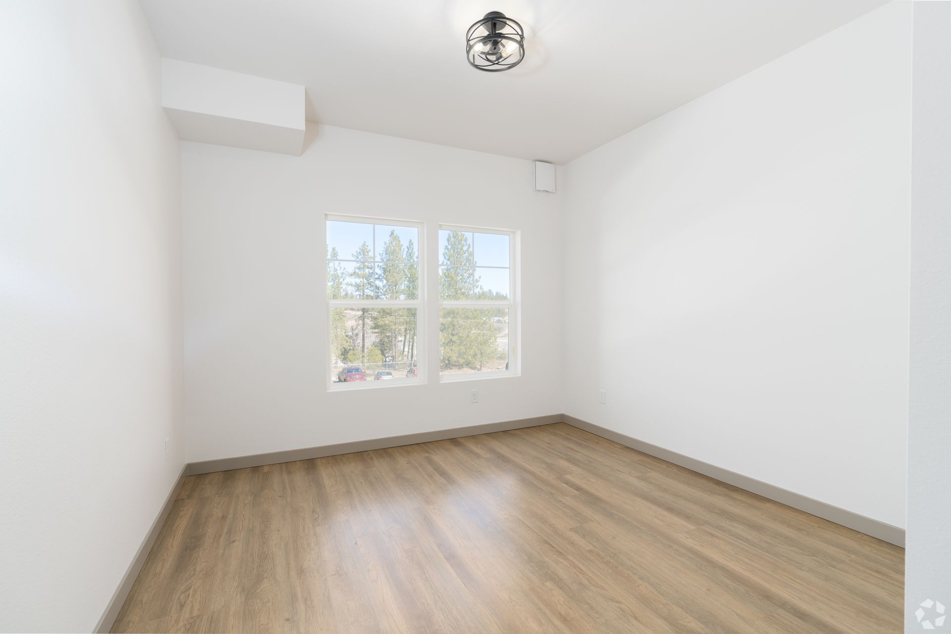 An empty room with hardwood floors and two windows.