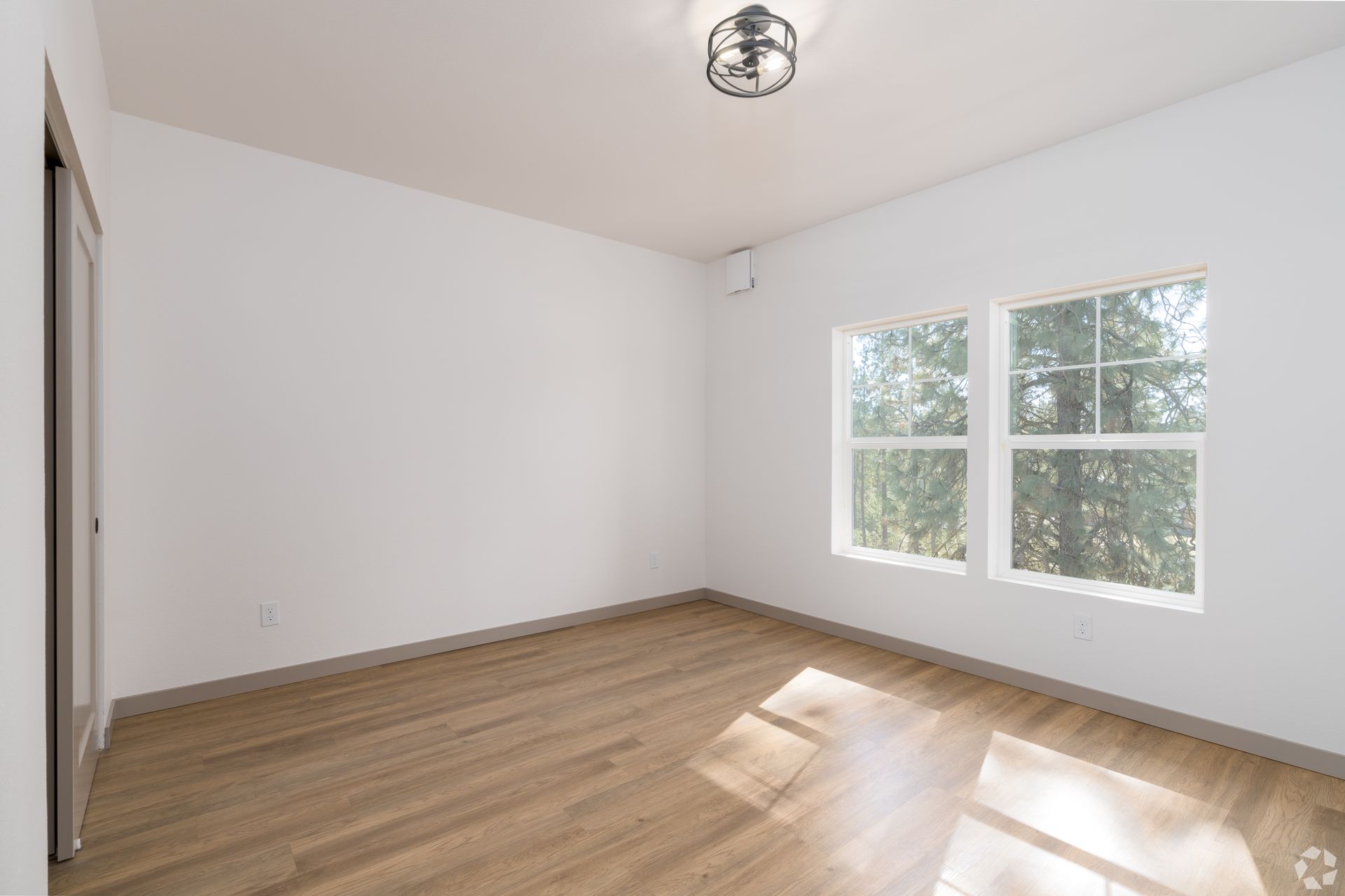 An empty room with hardwood floors and two windows.