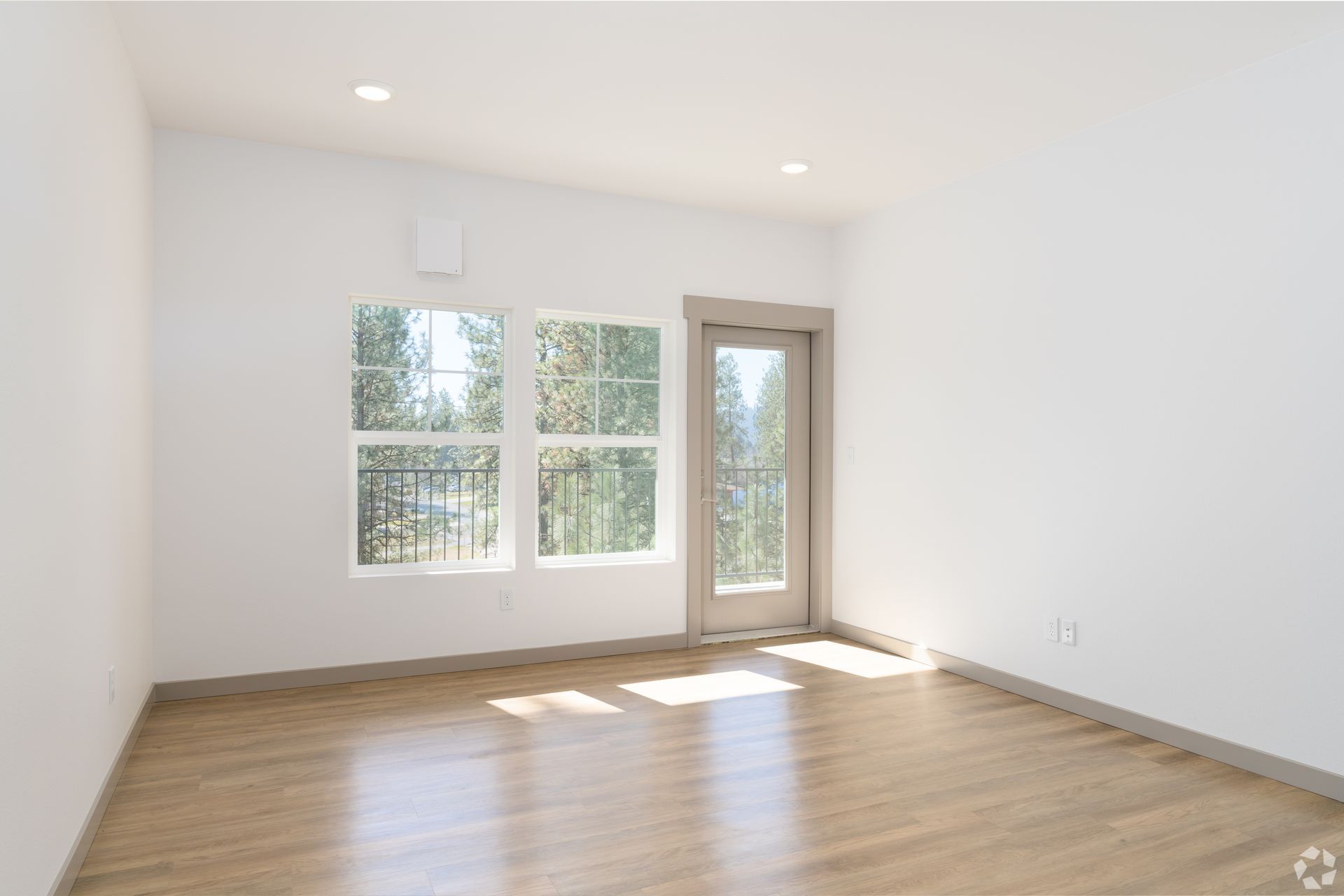 An empty living room with hardwood floors and white walls.