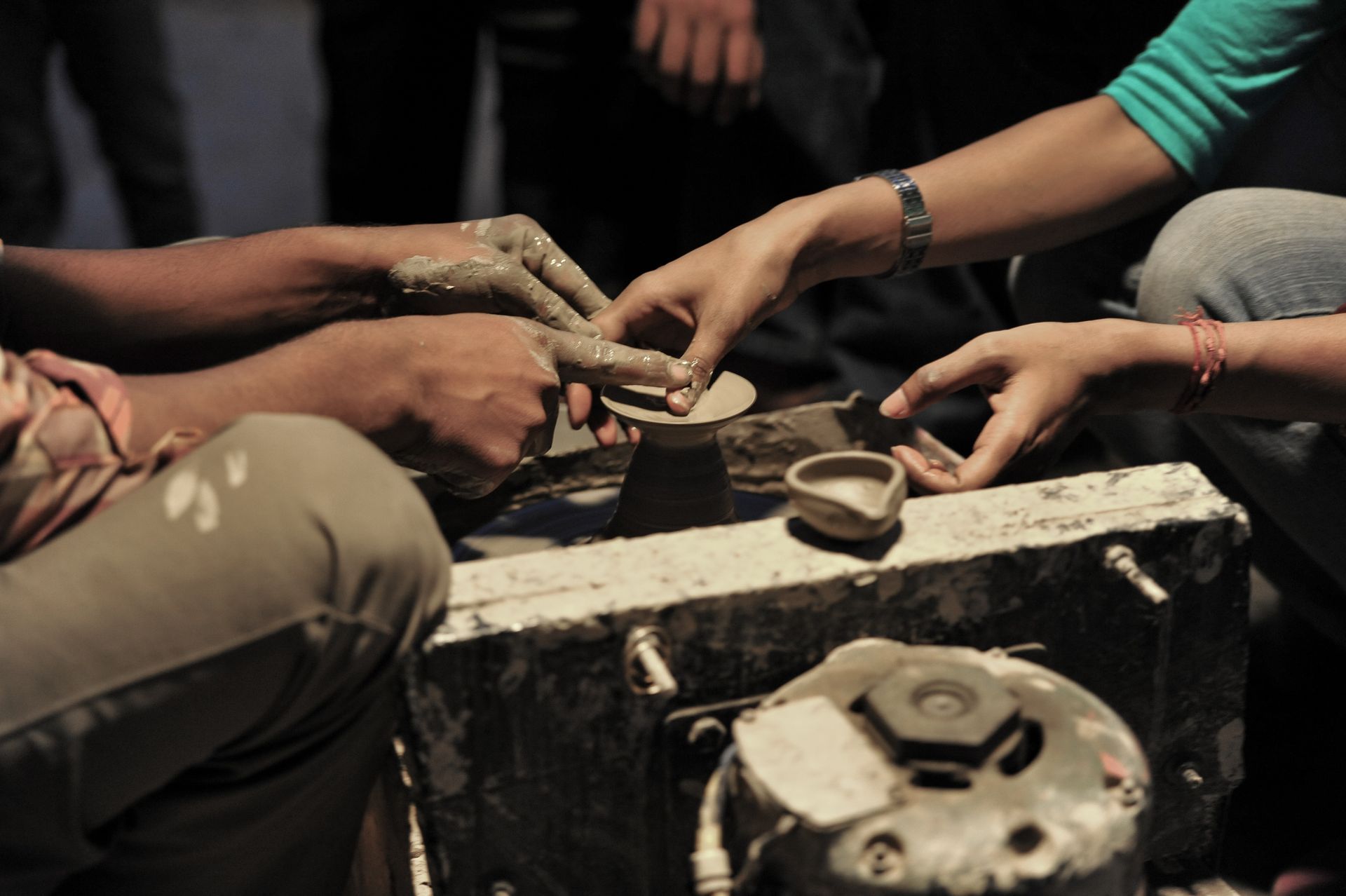 Hands shaping wet clay on a pottery wheel; two people work together.