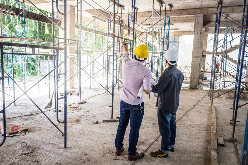 Two Construction Workers Are Looking At A Blueprint At A Construction Site — JTM Projects Australia Pty Ltd in Hollywell, QLD