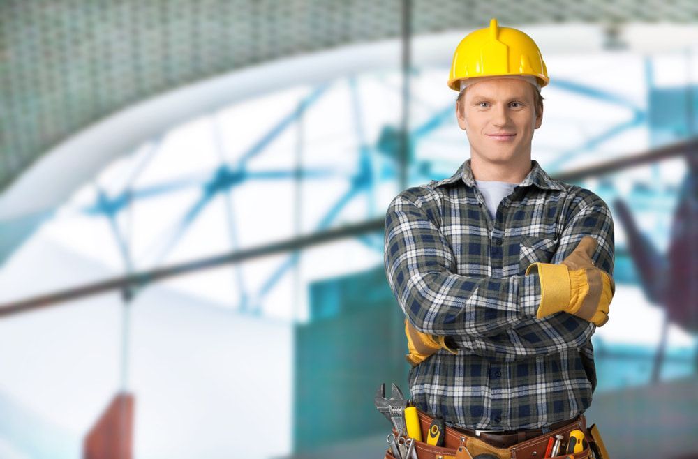 A Construction Worker Wearing A Hard Hat And Plaid Shirt Is Standing With His Arms Crossed — JTM Projects Australia Pty Ltd in Port Hedland, WA