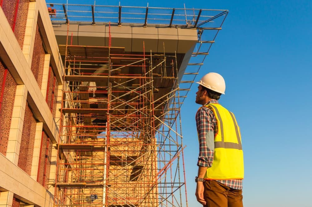 A Construction Worker Is Standing In Front Of A Building Under Construction — JTM Projects Australia Pty Ltd in Blackwater, QLD