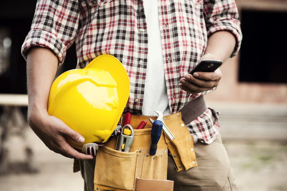 A Construction Worker Is Holding A Hard Hat And Looking At His Phone — JTM Projects Australia Pty Ltd in Brisbane, QLD