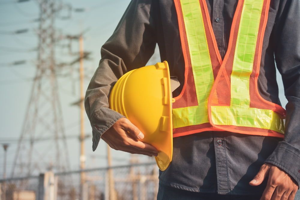 A Construction Worker Is Wearing A Safety Vest And Holding A Hard Hat — JTM Projects Australia Pty Ltd in Mackay, QLD