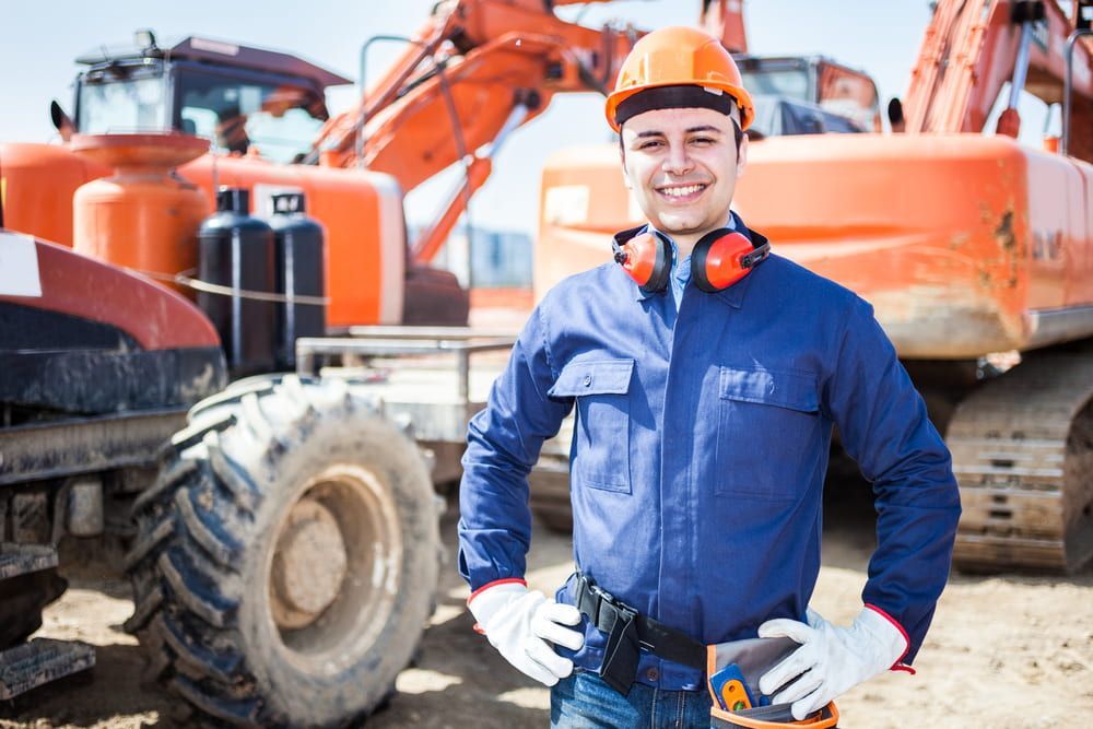 A Man In A Hard Hat Is Standing In Front Of A Construction Site — JTM Projects Australia Pty Ltd in Moranbah, QLD