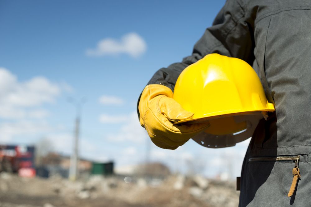 A Construction Worker Is Holding A Yellow Hard Hat And Gloves — JTM Projects Australia Pty Ltd in Townsville, QLD