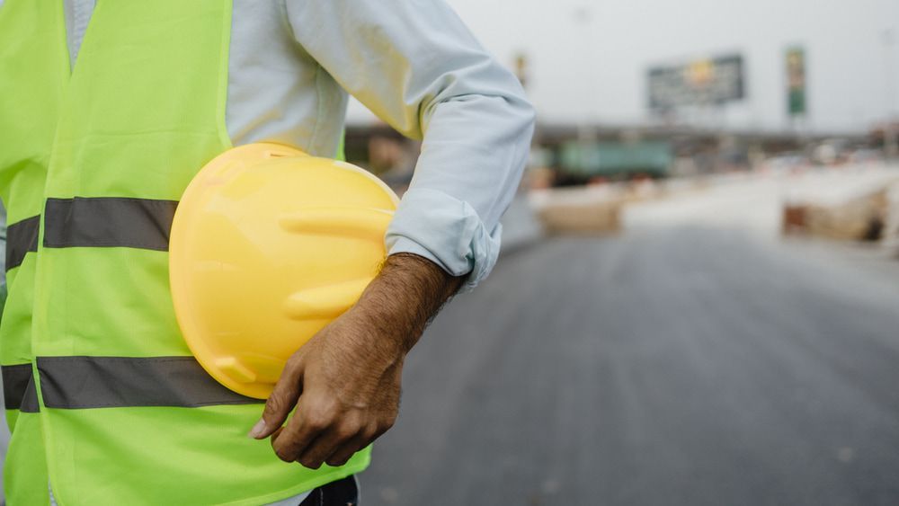 A Construction Worker Is Holding A Yellow Hard Hat In His Hand — JTM Projects Australia Pty Ltd in Gold Coast, QLD