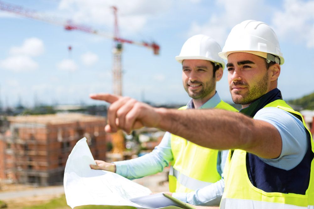 Two Construction Workers Are Looking At A Blueprint At A Construction Site — JTM Projects Australia Pty Ltd in Emerald, QLD