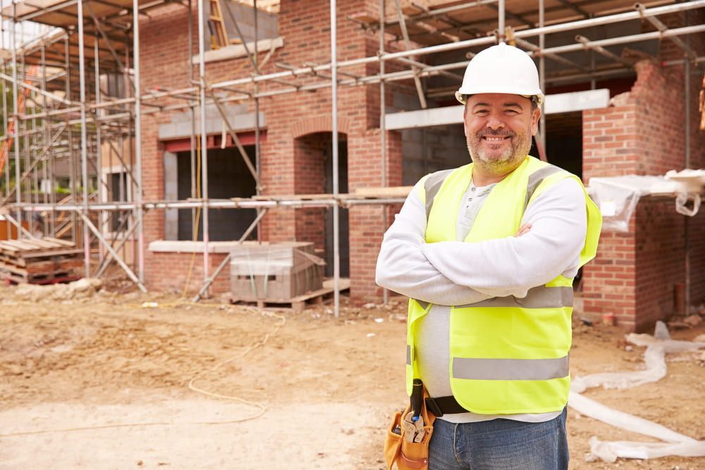 A Construction Worker Is Standing In Front Of A Brick Building Under Construction — JTM Projects Australia Pty Ltd in Brisbane, QLD