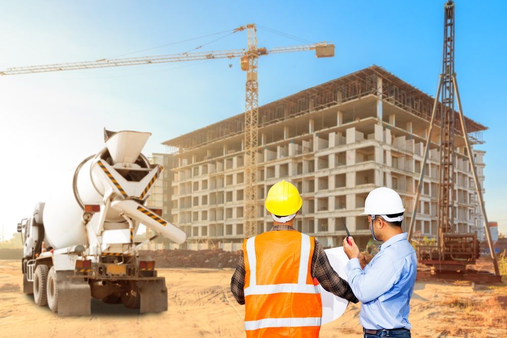 Two Construction Workers Are Looking At A Blueprint At A Construction Site — JTM Projects Australia Pty Ltd in Blackwater, QLD