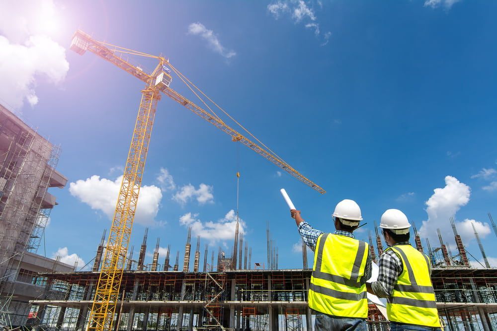 Two Construction Workers Are Looking At A Crane At A Construction Site — JTM Projects Australia Pty Ltd in Townsville, QLD
