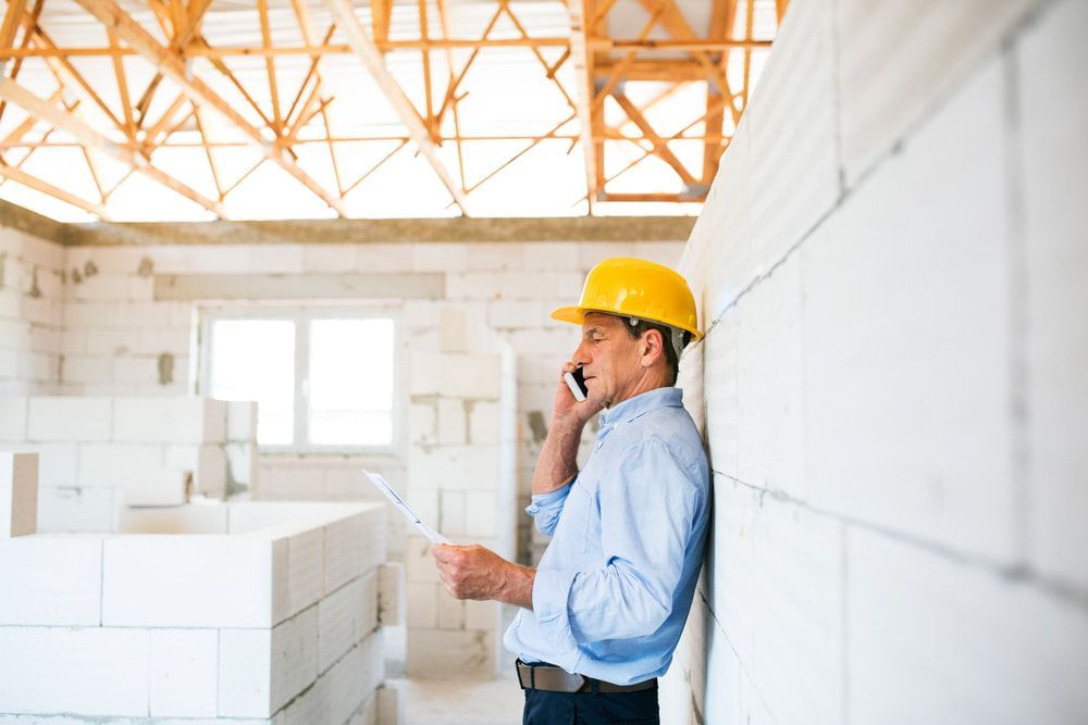 A Construction Worker Is Leaning Against A Wall While Talking On A Cell Phone — JTM Projects Australia Pty Ltd in Gold Coast, QLD
