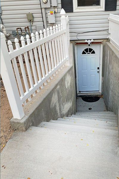 Concrete stairs lead down to a white door. A white picket fence runs along the left side.