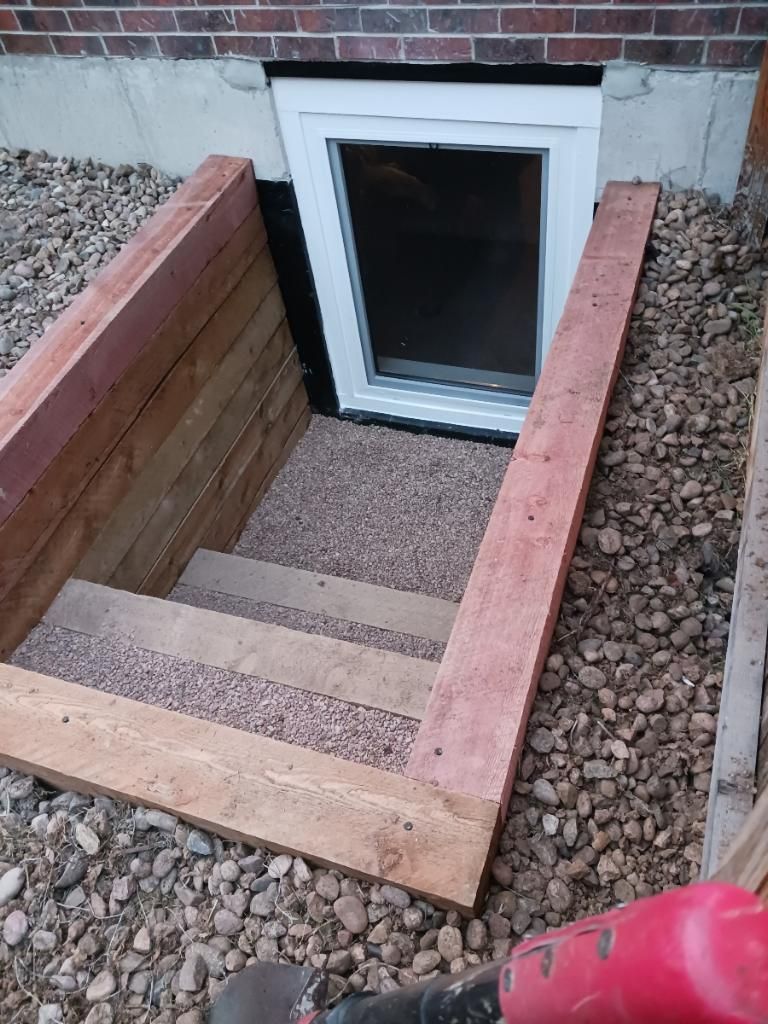 Excavation against a building's foundation wall. Brown dirt and gravel surround the hole. The wall is concrete.