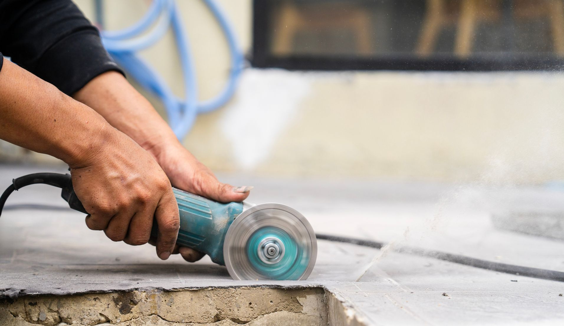 Blocks of concrete and gravel are piled on a curb next to a parking space near a building with a blue dumpster in the background.