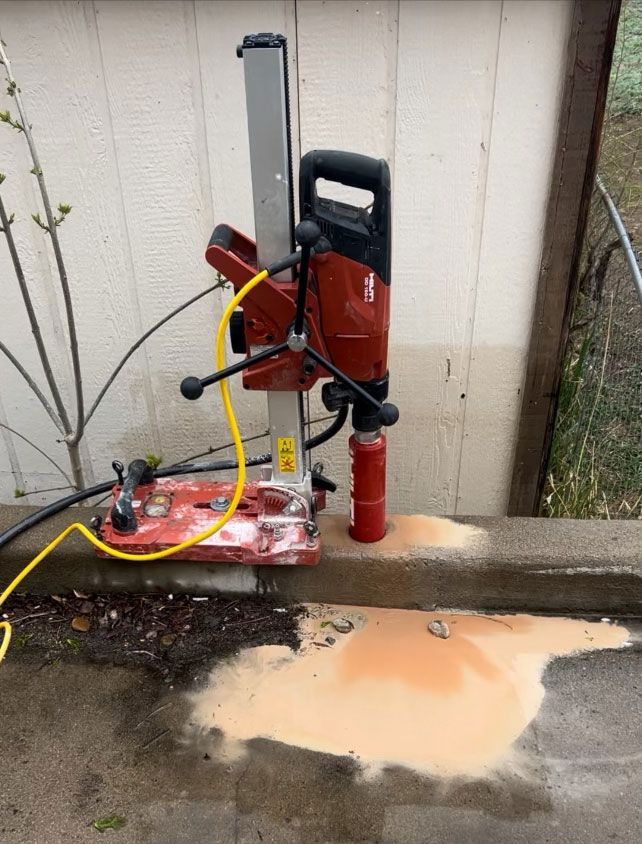 A concrete core drilling machine is set up to drill into a concrete surface, creating a pool of slurry.