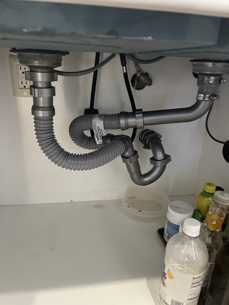 A kitchen sink with a hose underneath it and a bottle of water.