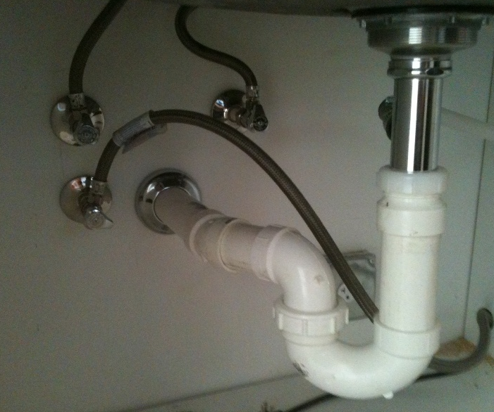 A white pipe under a sink with a hose attached to it