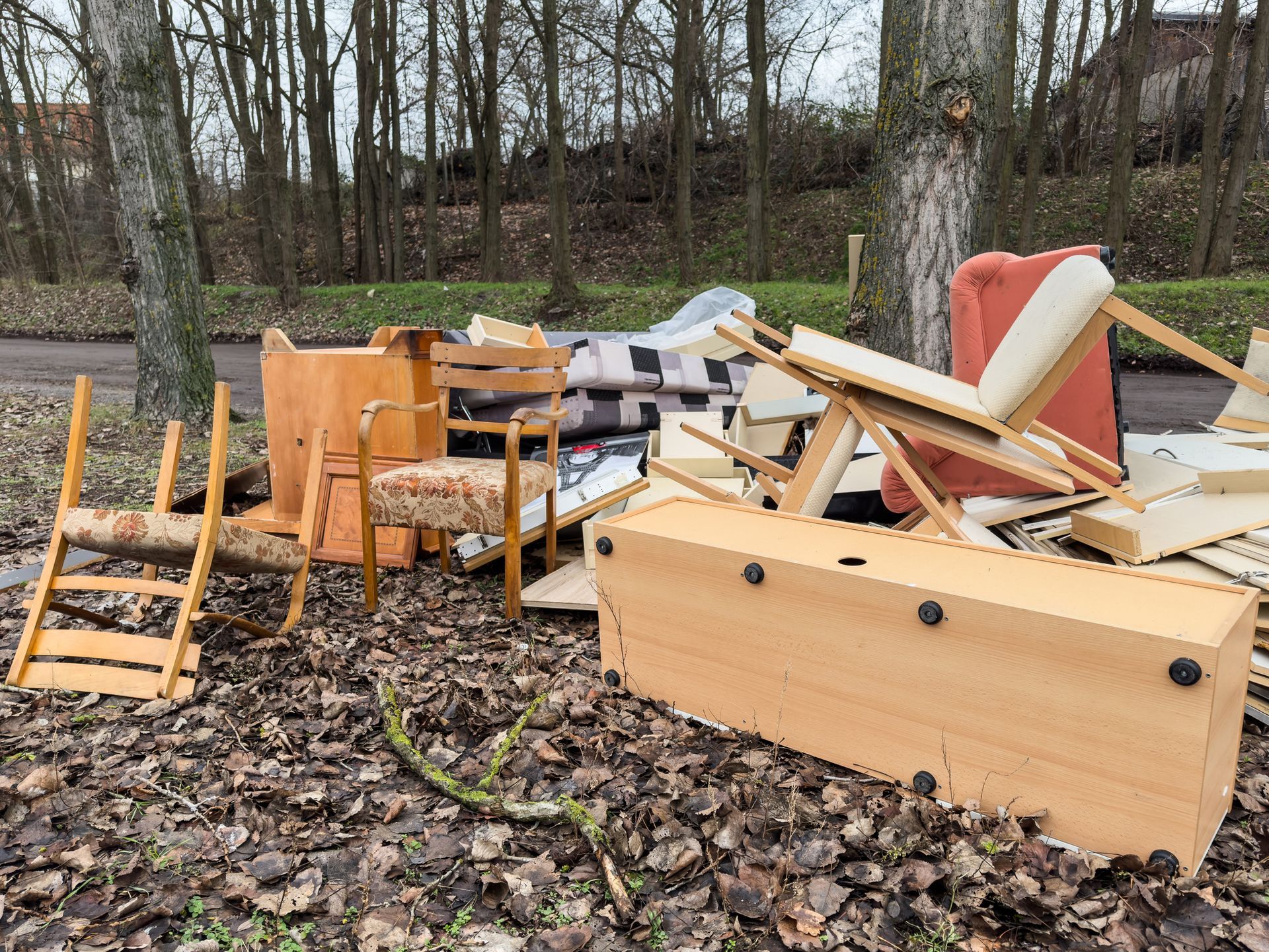 Pile of discarded furniture, including chairs and a dresser, left outdoors on leaves.