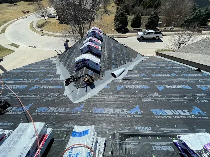 Roofer on a home roof replacing shingles, near a street and vehicles.
