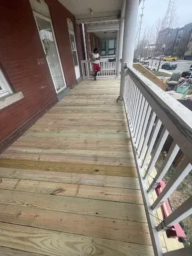 Wooden deck with a person standing on it, red brick building in background.