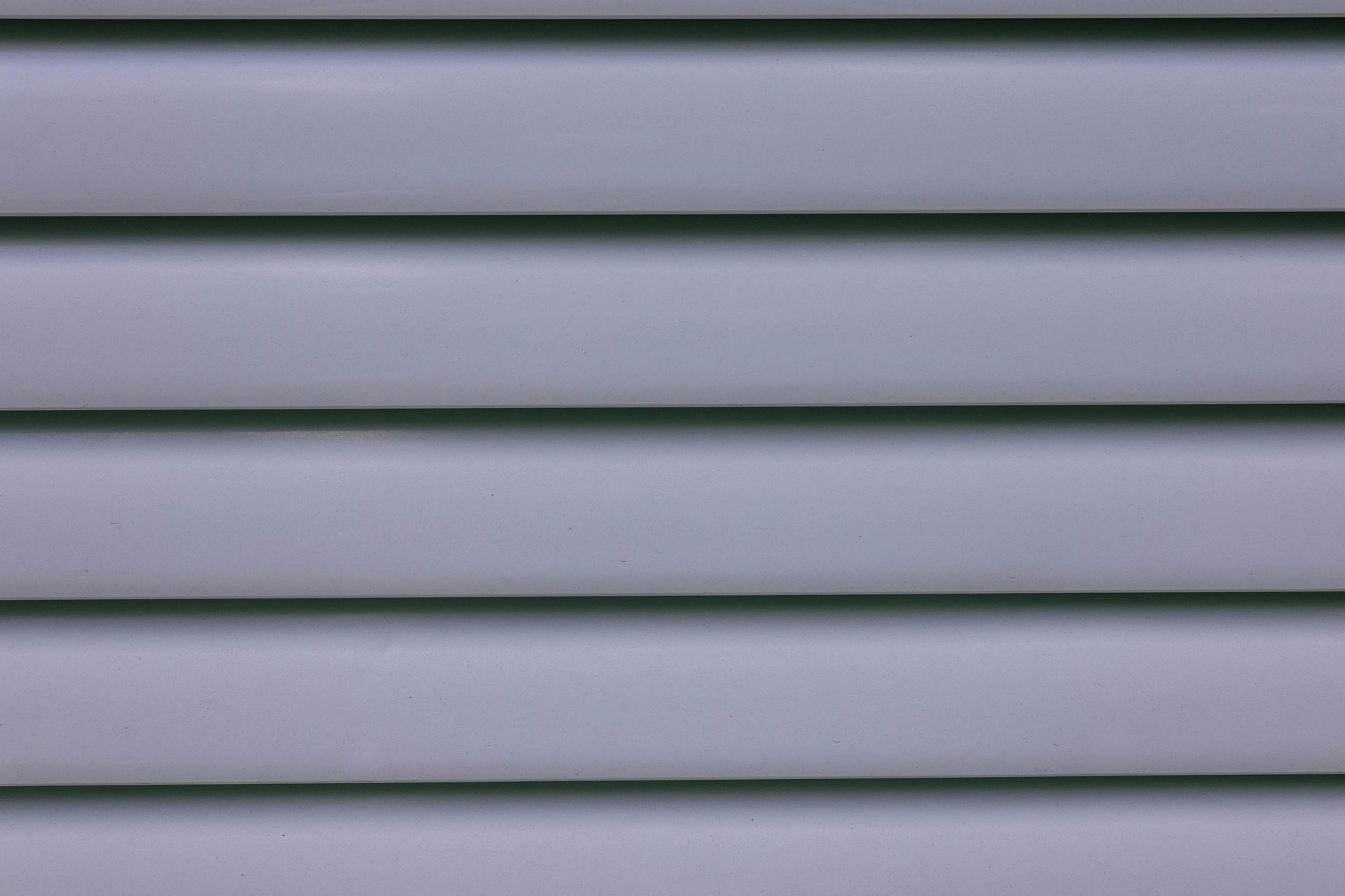 Close-up of light gray horizontal siding with raised, parallel ridges.