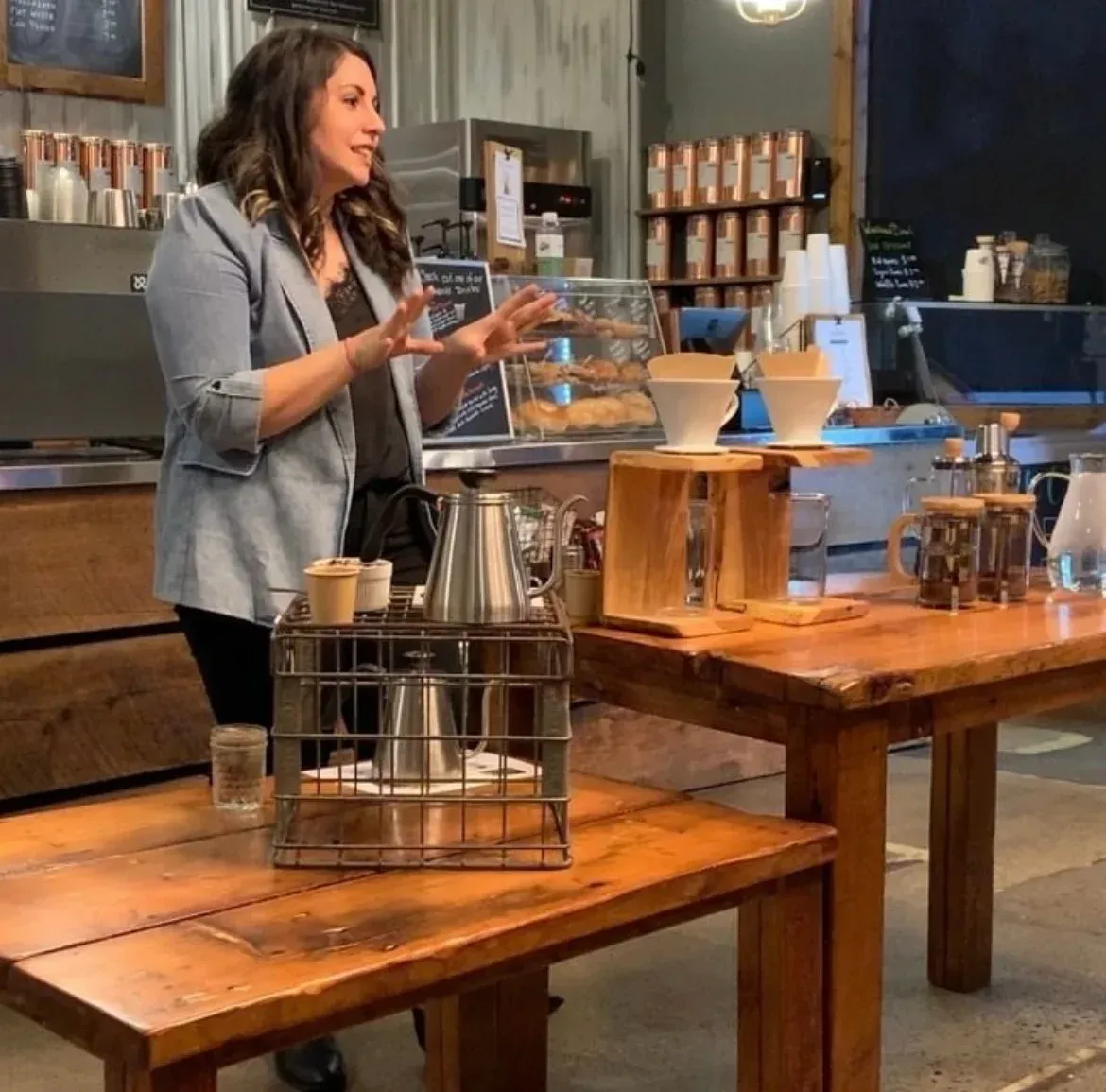 A woman in a blue jacket is standing in front of wooden tables