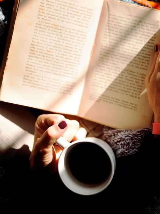 A woman is holding a cup of coffee and reading a book