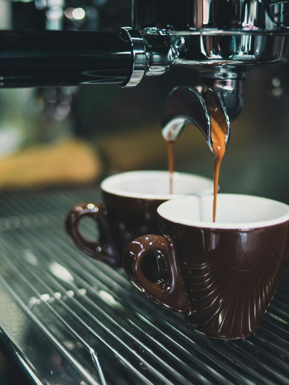 Two cups of coffee are being poured from a coffee machine