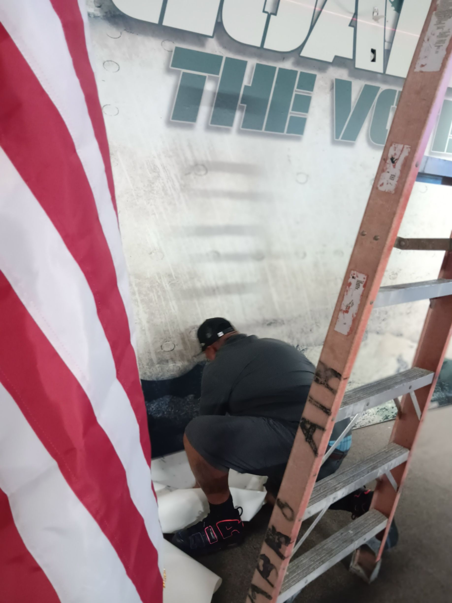 A man sits on a ladder in front of a sign that says juan the vio