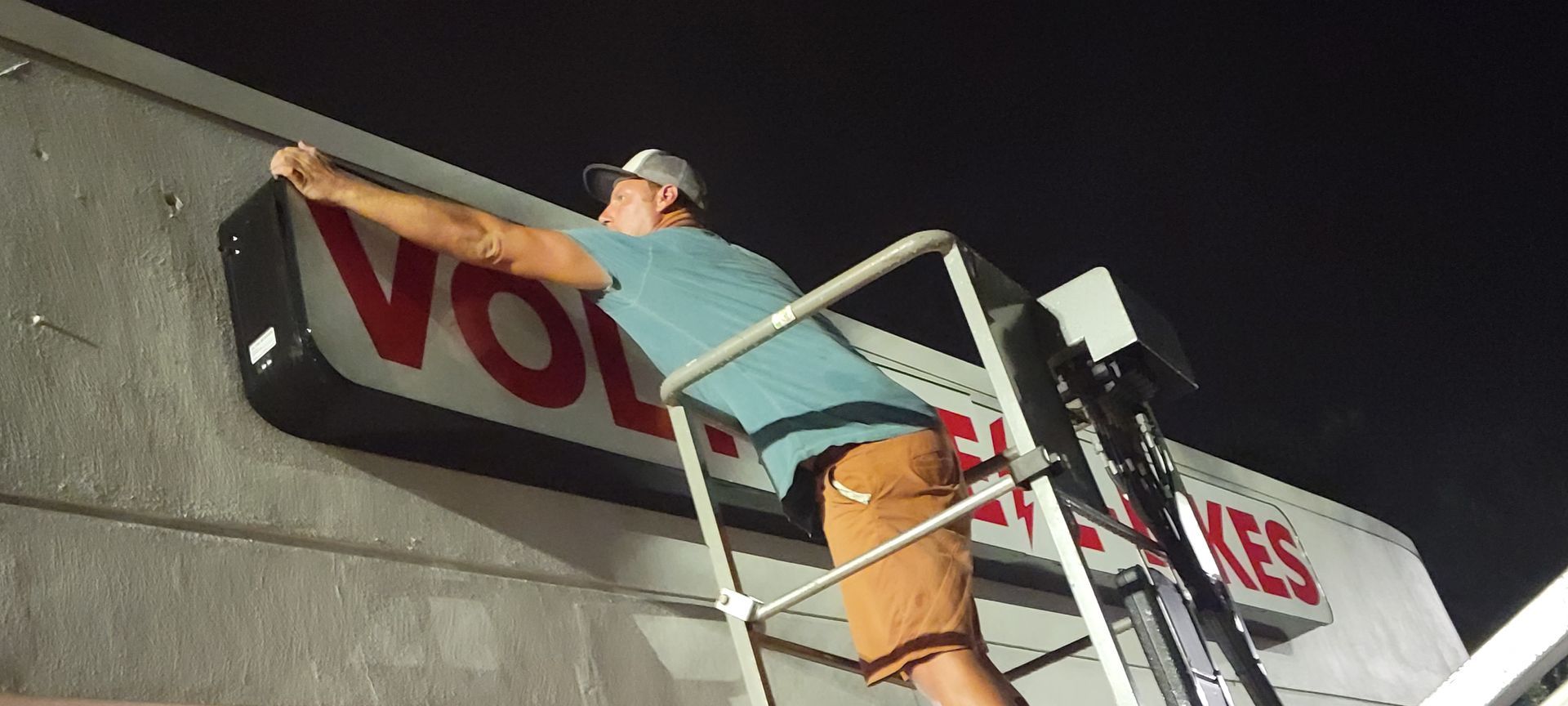 A man is standing on a ladder hanging a sign on a building.