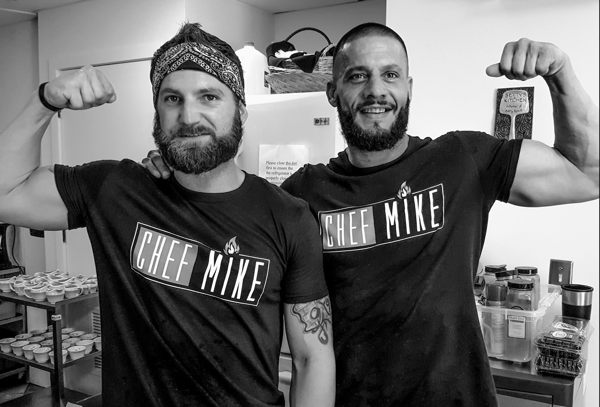 Two men wearing chef mike shirts are flexing their muscles