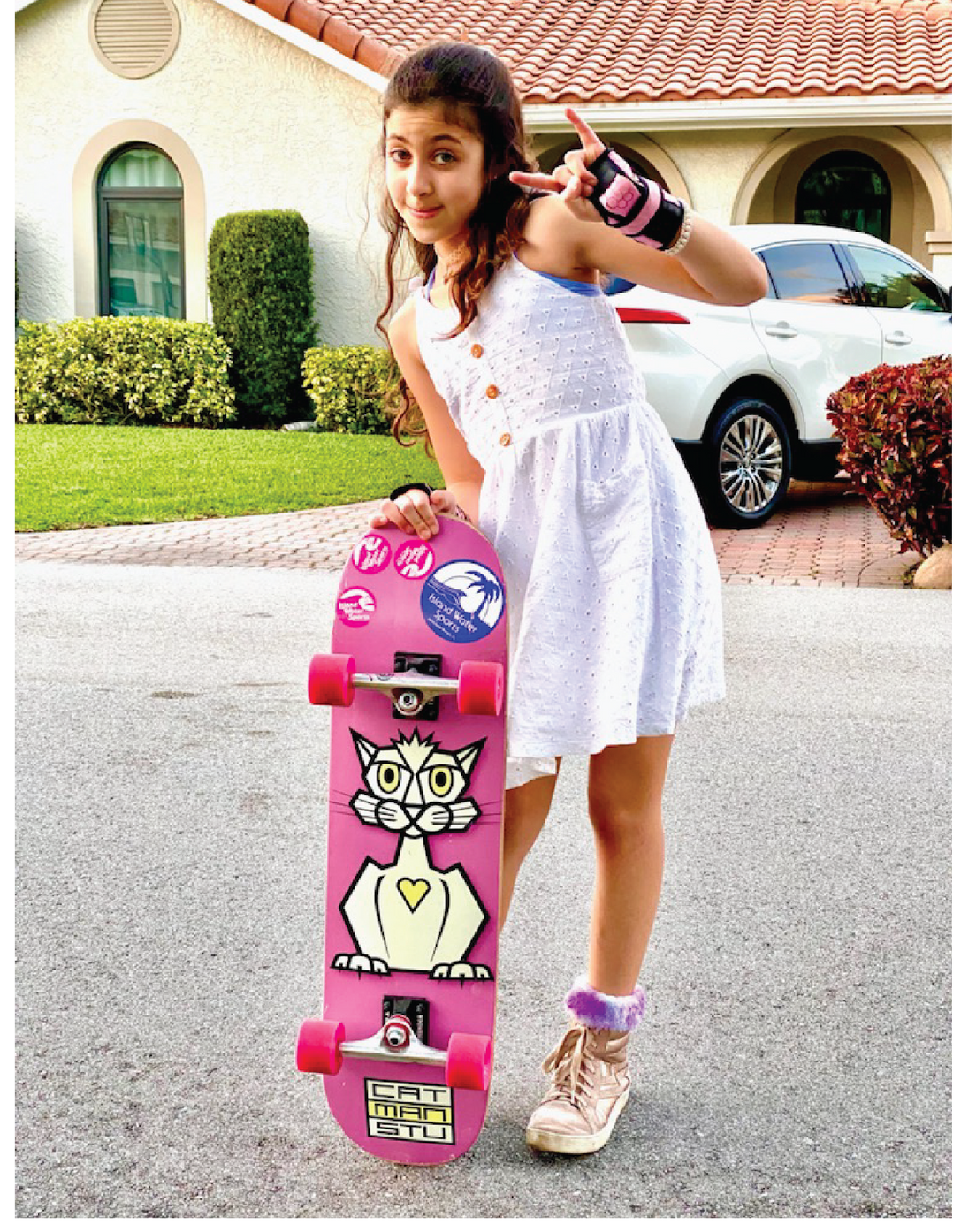 A young girl holding a pink catmanstu skateboard.