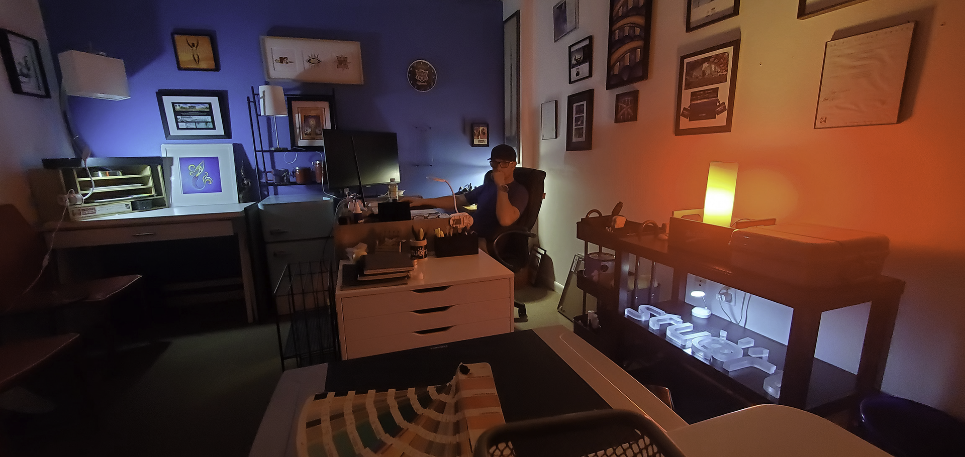 A man is sitting at a desk in a living room with a fireplace.