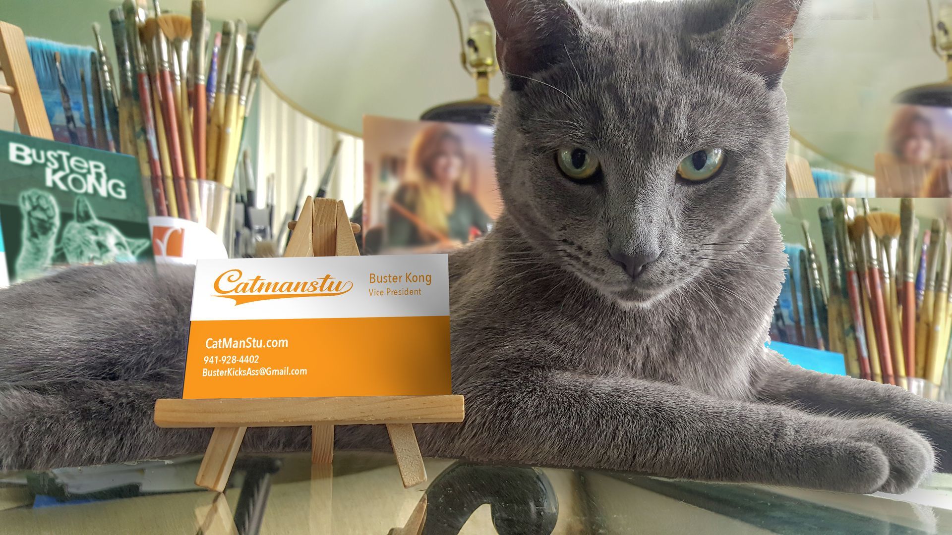 A cat laying on a table next to a business card that says Catmanstu.