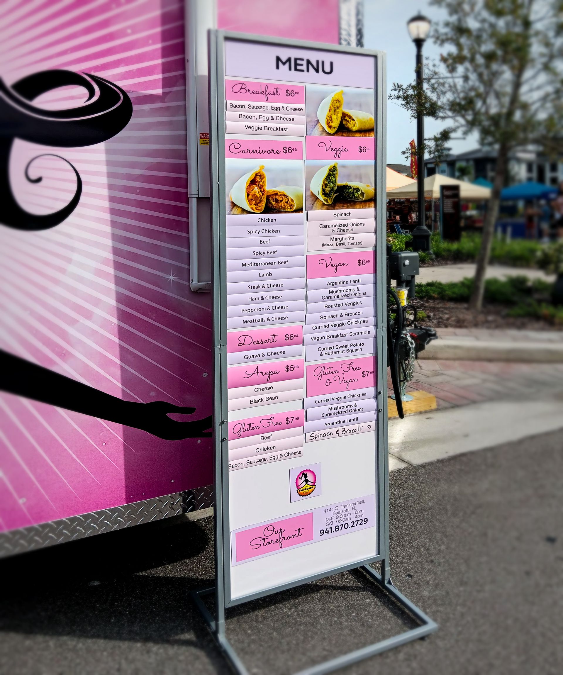 A menu is displayed in front of a pink food truck