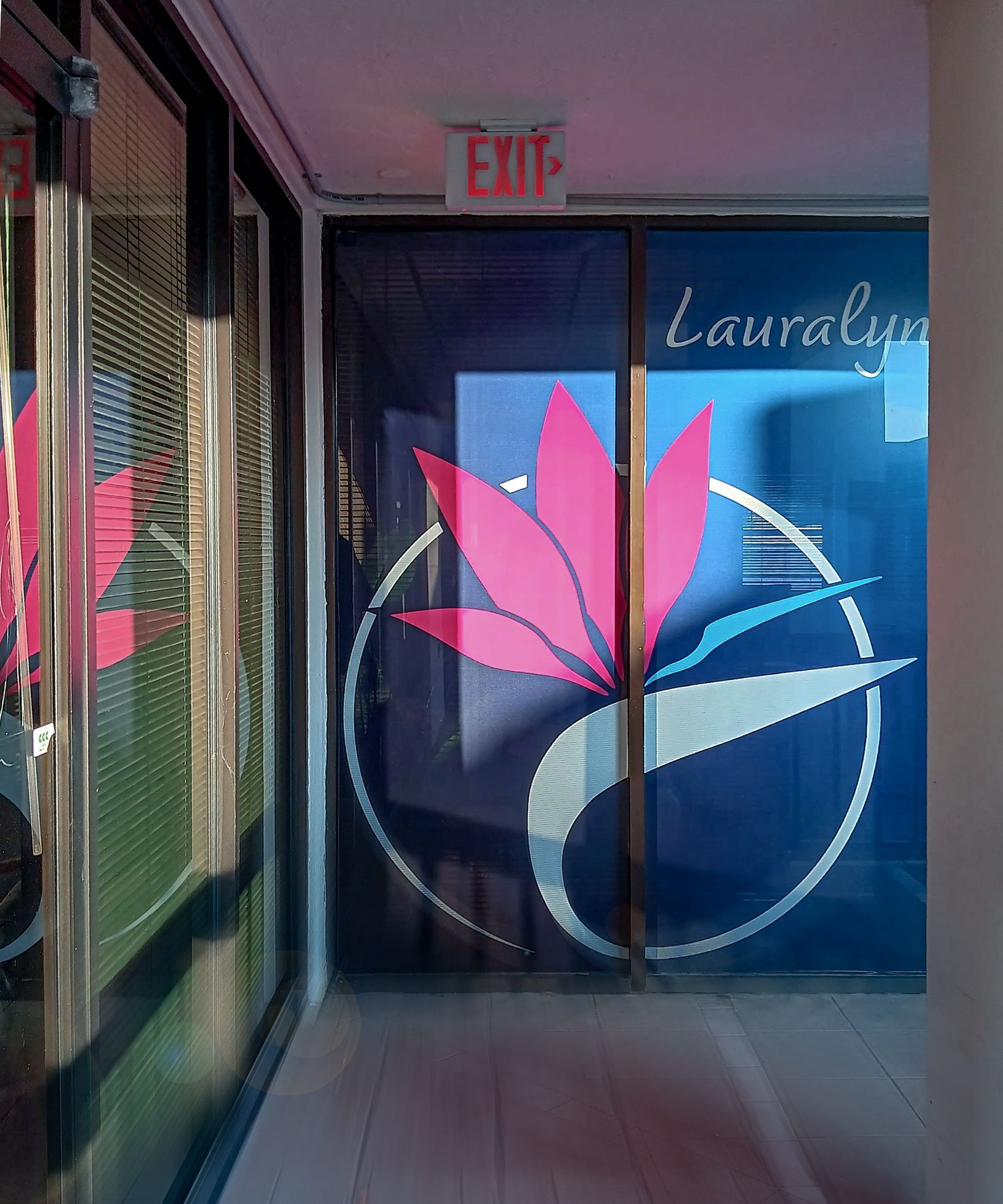 An exit sign is above a glass door with a pink flower on it