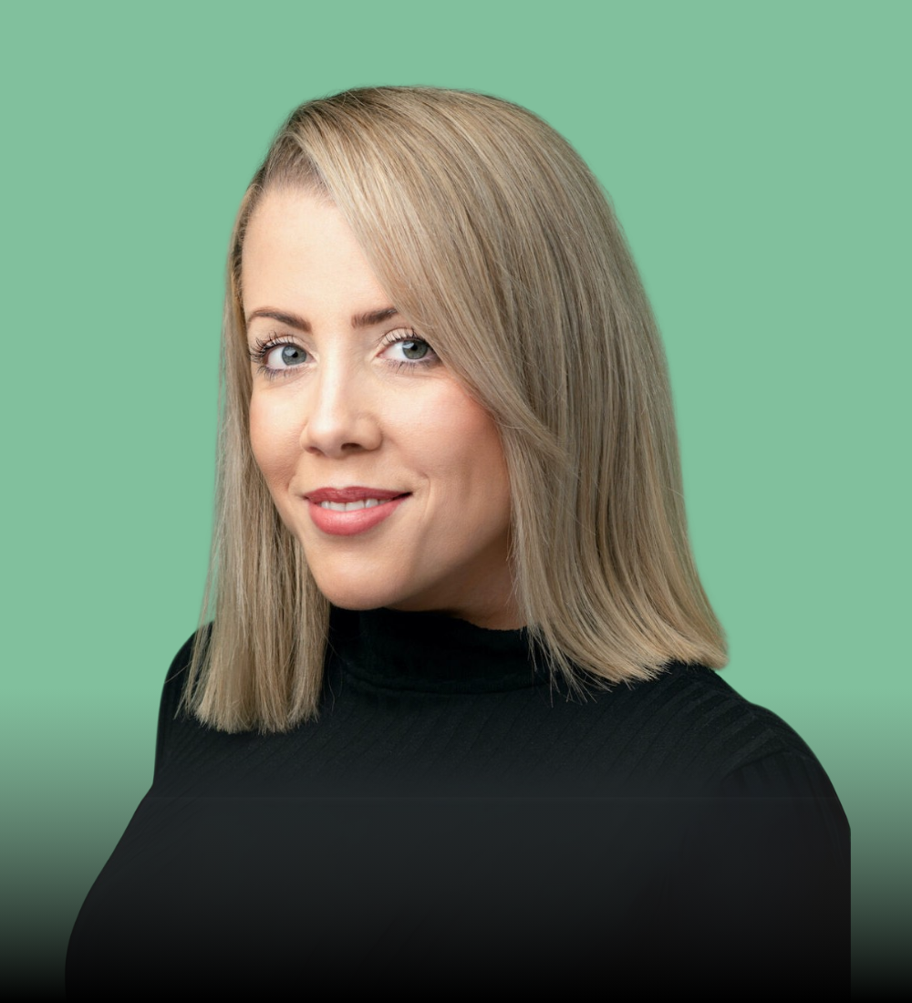 A woman with blonde hair is wearing a black turtleneck and smiling.